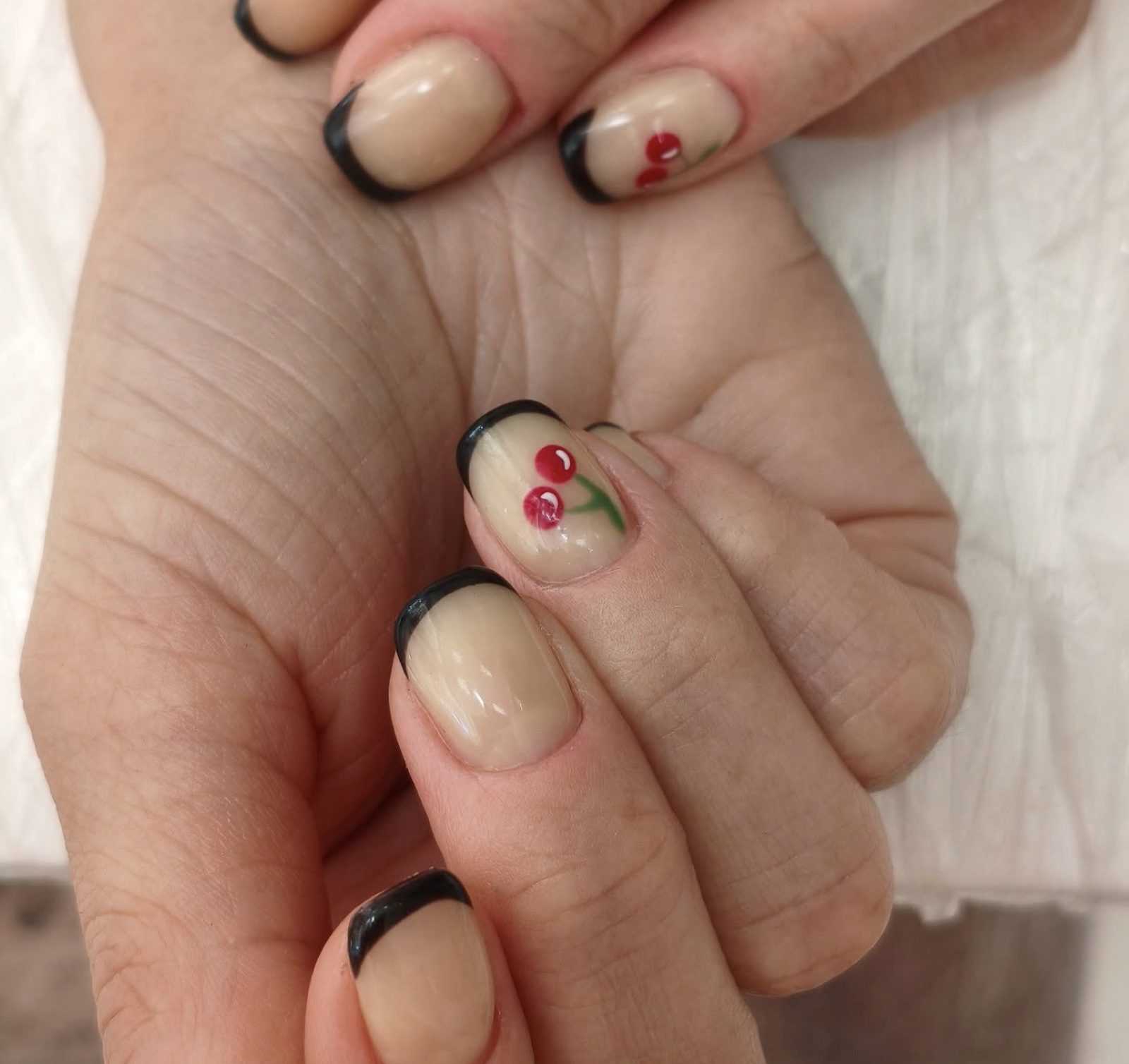 Nude short square manicure with black French tips and hand-painted red cherry accent nail